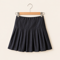 Classic black cotton box pleat skirt for girls with structured pleats hanging on a wooden hanger
