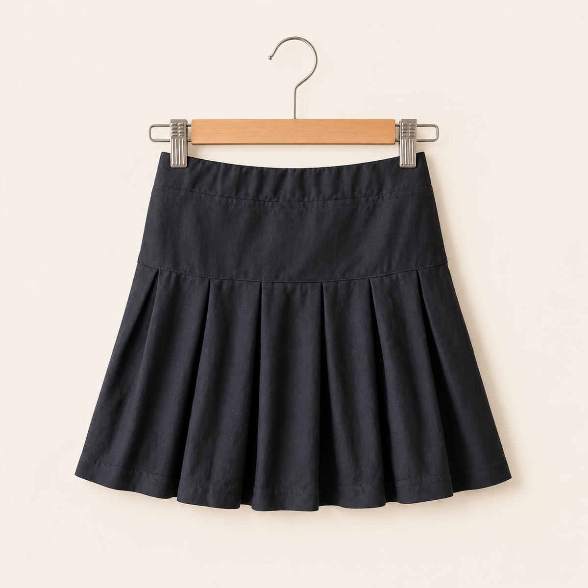 Classic black cotton box pleat skirt for girls with structured pleats hanging on a wooden hanger